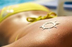 Espalda de una mujer tomando el sol con un bikini amarillo y dibujo de un sol hecho con crema solar, imagen asociada a protección cutánea y nutriacéuticos.